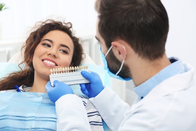 Dentist matching patient's teeth color with palette in office