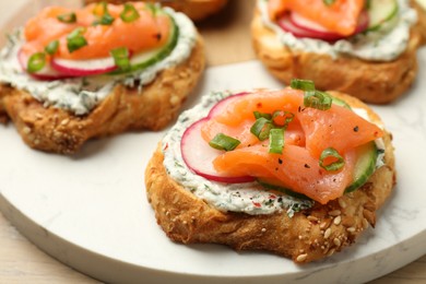 Tasty canapes with salmon, cucumber, radish and cream cheese on table, closeup