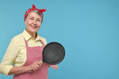 Photo of Happy housewife with frying pan on light blue background, space for text