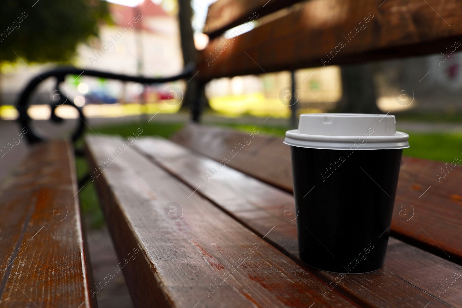 Photo of Takeaway paper cup with plastic lid on wooden bench outdoors, space for text