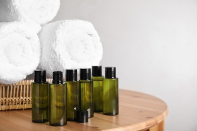 Mini bottles with cosmetic products and towels on wooden table against light background. Space for text