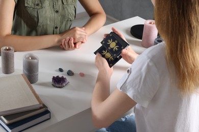 Astrologer predicting client's future with tarot cards at table indoors, closeup