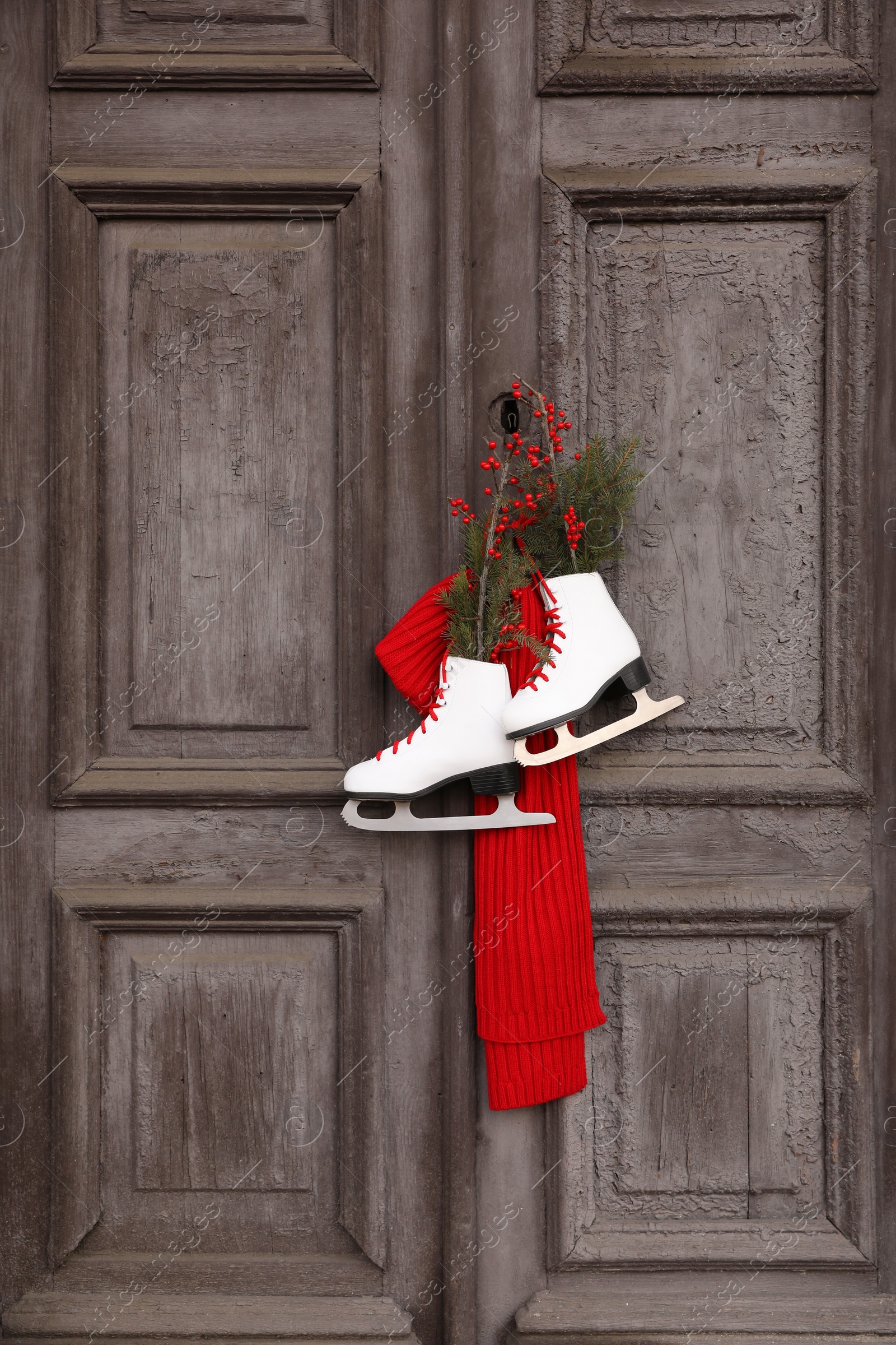 Photo of Pair of ice skates with Christmas decor hanging on old wooden door