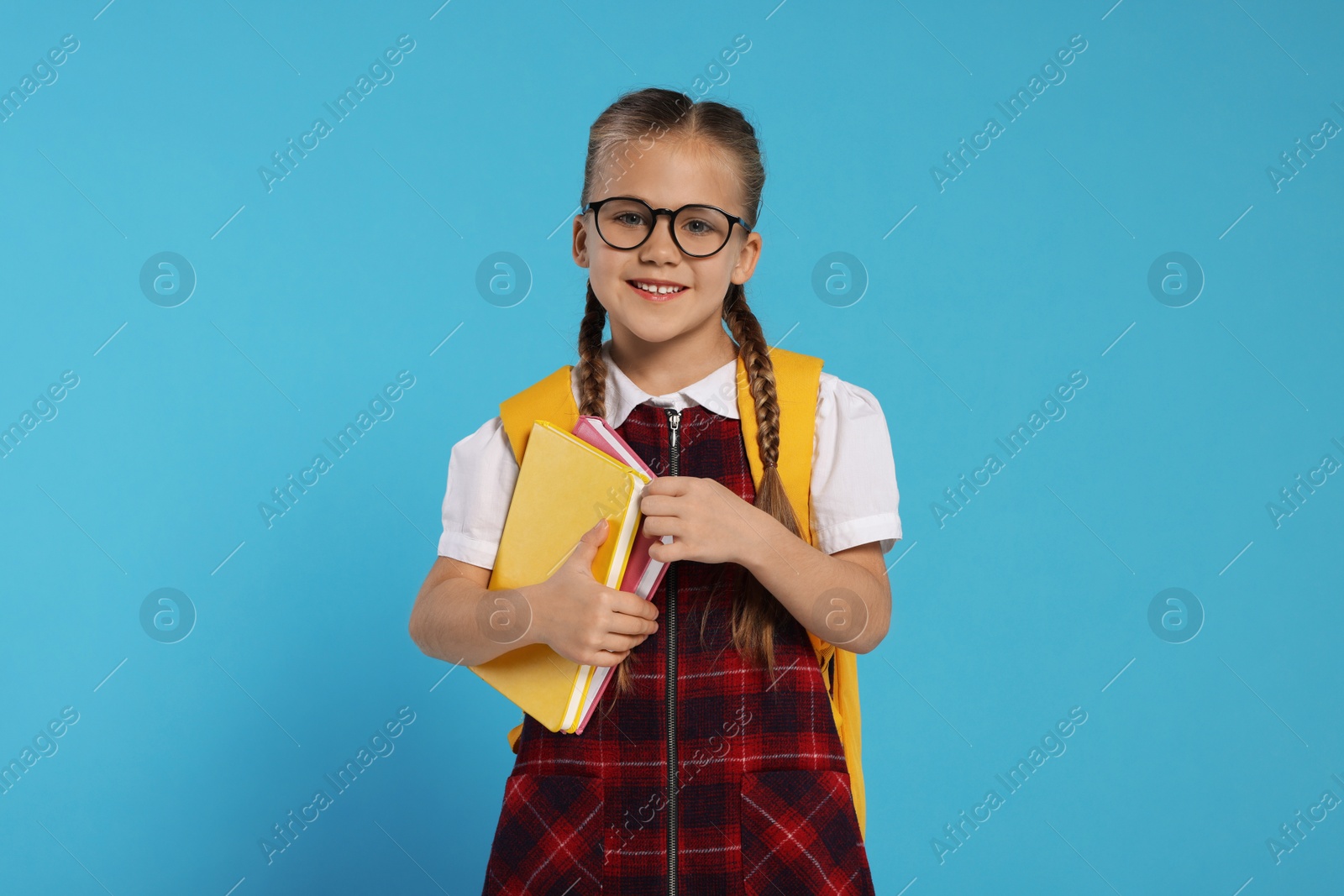 Photo of Happy schoolgirl in glasses with backpack and books on light blue background