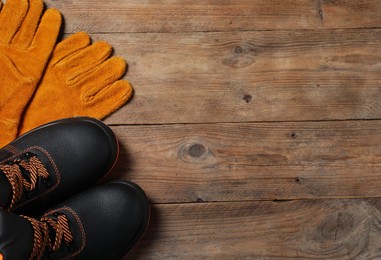 Photo of Pair of working boots and protective gloves on wooden surface, top view. Space for text