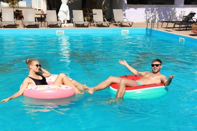 Happy young couple with inflatable rings in swimming pool