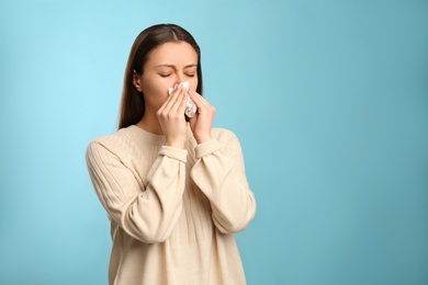 Photo of Young woman with tissue suffering from runny nose on light blue background. Space for text