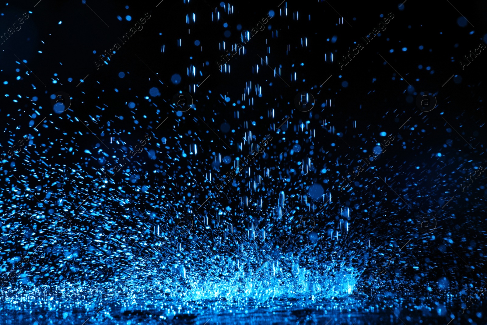 Photo of Heavy rain falling down on ground against dark background, toned in blue