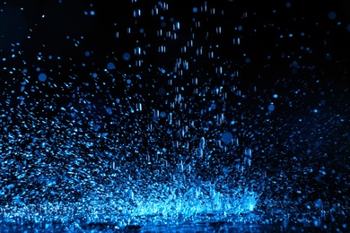 Photo of Heavy rain falling down on ground against dark background, toned in blue