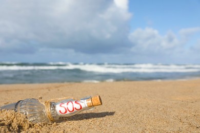 Photo of Glass bottle with SOS message on sand near sea, space for text