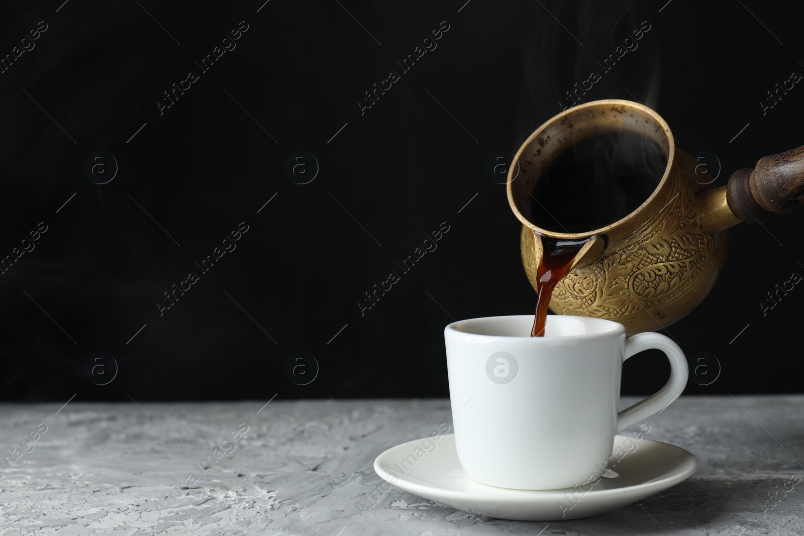 Photo of Turkish coffee. Pouring brewed beverage from cezve into cup at grey table. Space for text