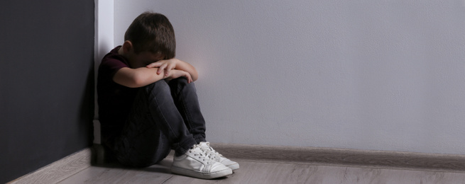 Sad little boy sitting on floor indoors, banner design with space for text. Time to visit child psychologist