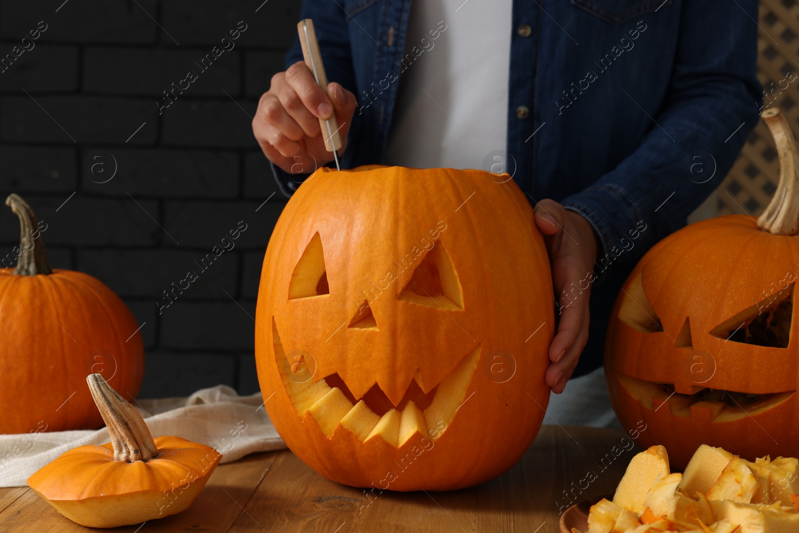 Photo of Woman carving pumpkin at wooden table, closeup. Halloween celebration