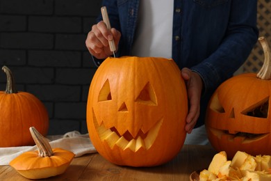 Woman carving pumpkin at wooden table, closeup. Halloween celebration