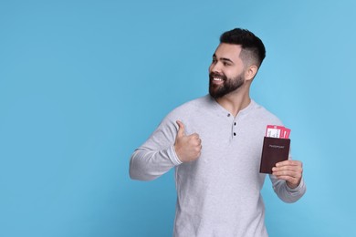 Happy man with passport and tickets showing thumb up on light blue background. Space for text