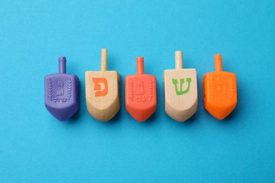 Photo of Different dreidels on light blue background, flat lay. Traditional Hanukkah game