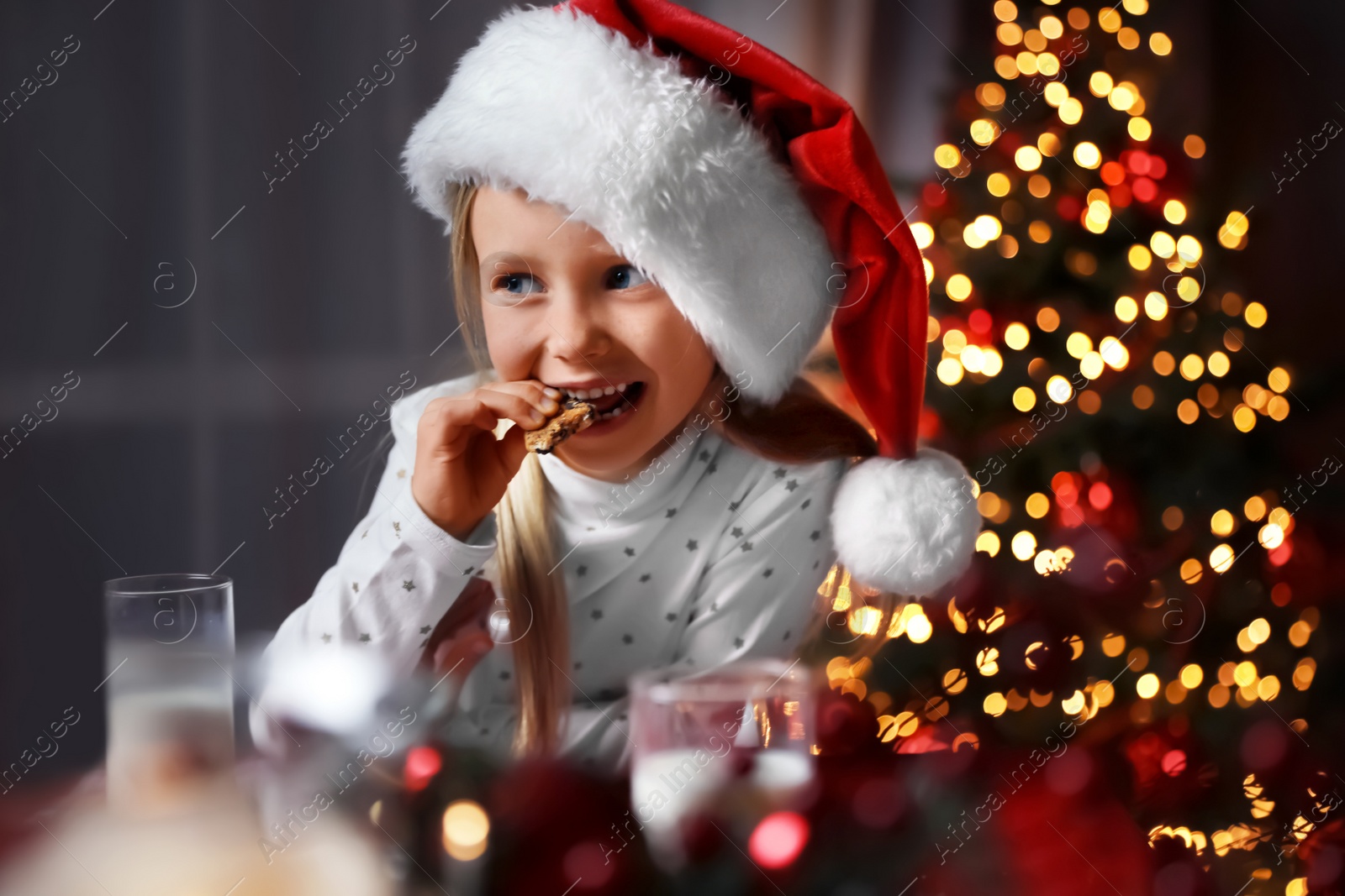 Photo of Cute little child eating cookies at table in dining room. Christmas time