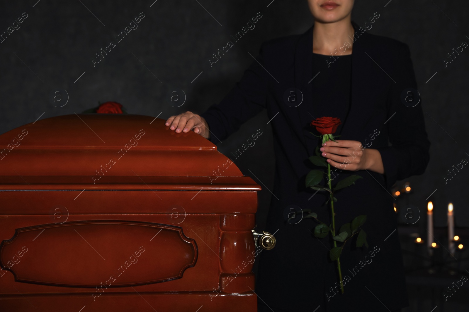 Photo of Young woman with red rose near casket in funeral home, closeup