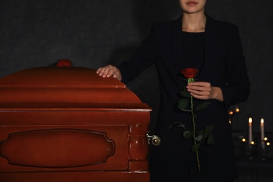 Young woman with red rose near casket in funeral home, closeup