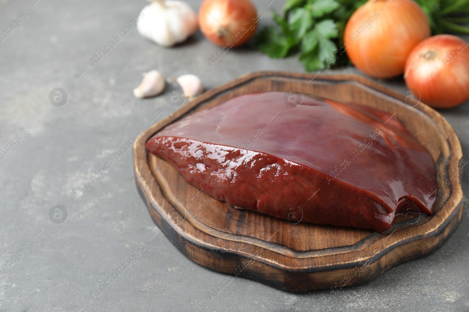 Photo of Piece of raw beef liver and products on grey table, closeup. Space for text