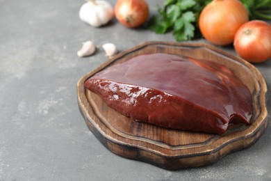 Photo of Piece of raw beef liver and products on grey table, closeup. Space for text