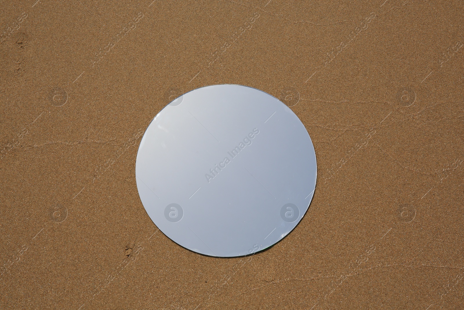 Photo of Round mirror reflecting sky on sand outdoors, top view