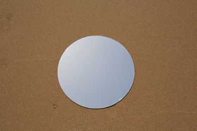 Round mirror reflecting sky on sand outdoors, top view