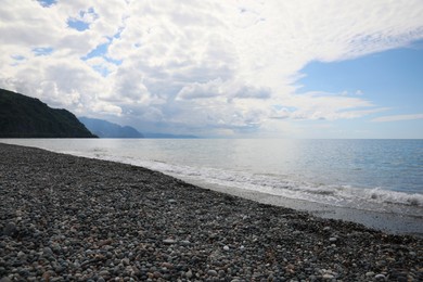 Photo of Picturesque view of beautiful sea shore and mountains under sky with fluffy clouds