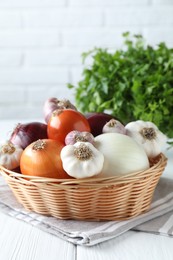 Fresh raw garlic and onions in wicker basket on white table