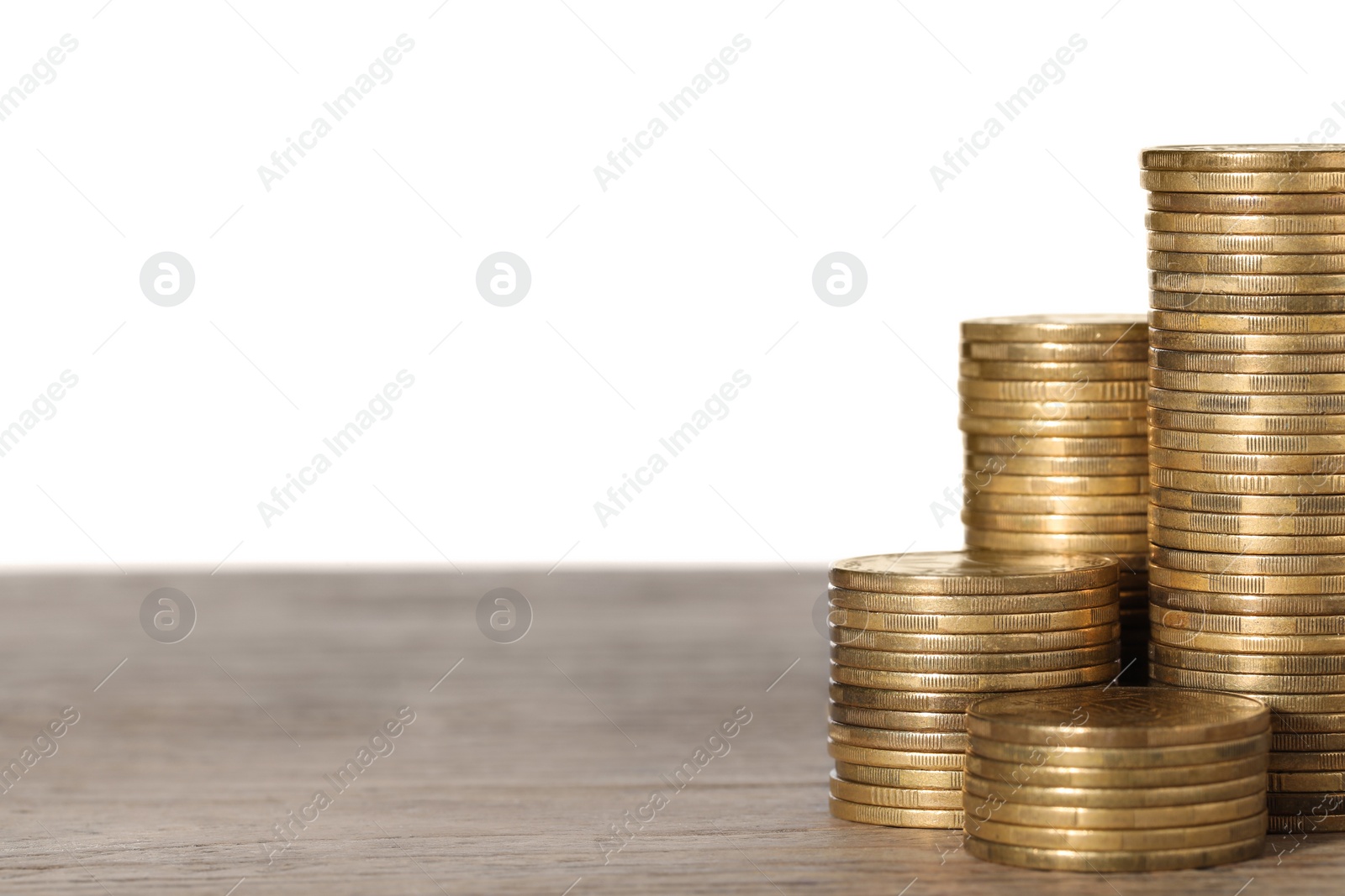 Photo of Many golden coins stacked on wooden table against white background, space for text