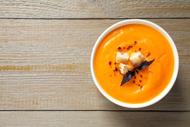 Delicious pumpkin soup in bowl on wooden table, top view. Space for text