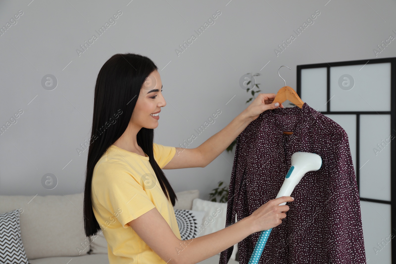 Photo of Woman steaming blouse on hanger at home