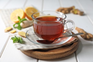 Photo of Cup of delicious ginger tea and ingredients on white wooden table, closeup