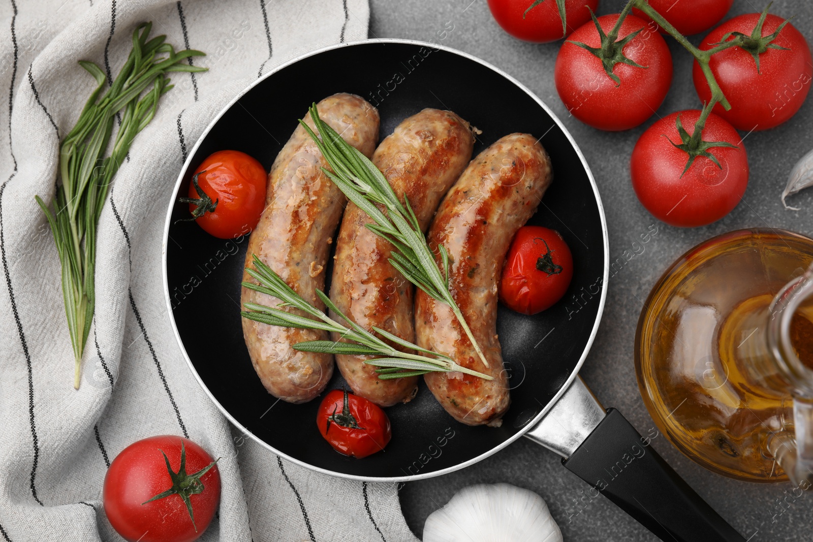 Photo of Frying pan with tasty homemade sausages, rosemary and tomatoes on brown textured table, flat lay