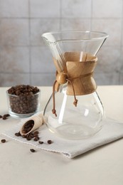 Empty glass chemex coffeemaker with and beans on white table