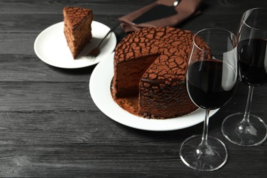 Photo of Delicious chocolate truffle cake and red wine on black wooden table, space for text