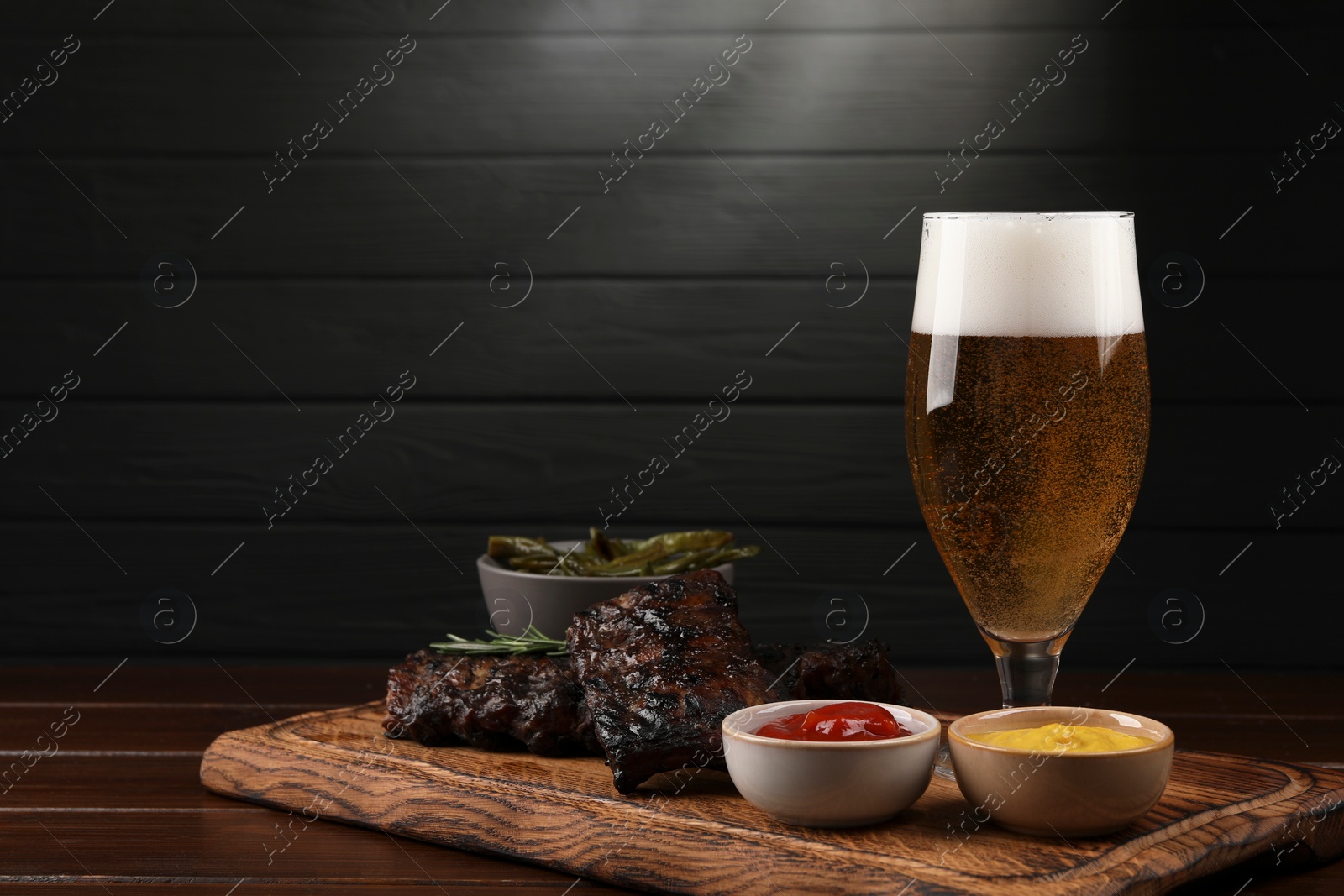 Photo of Glass of beer, delicious grilled ribs and sauces on wooden table. Space for text