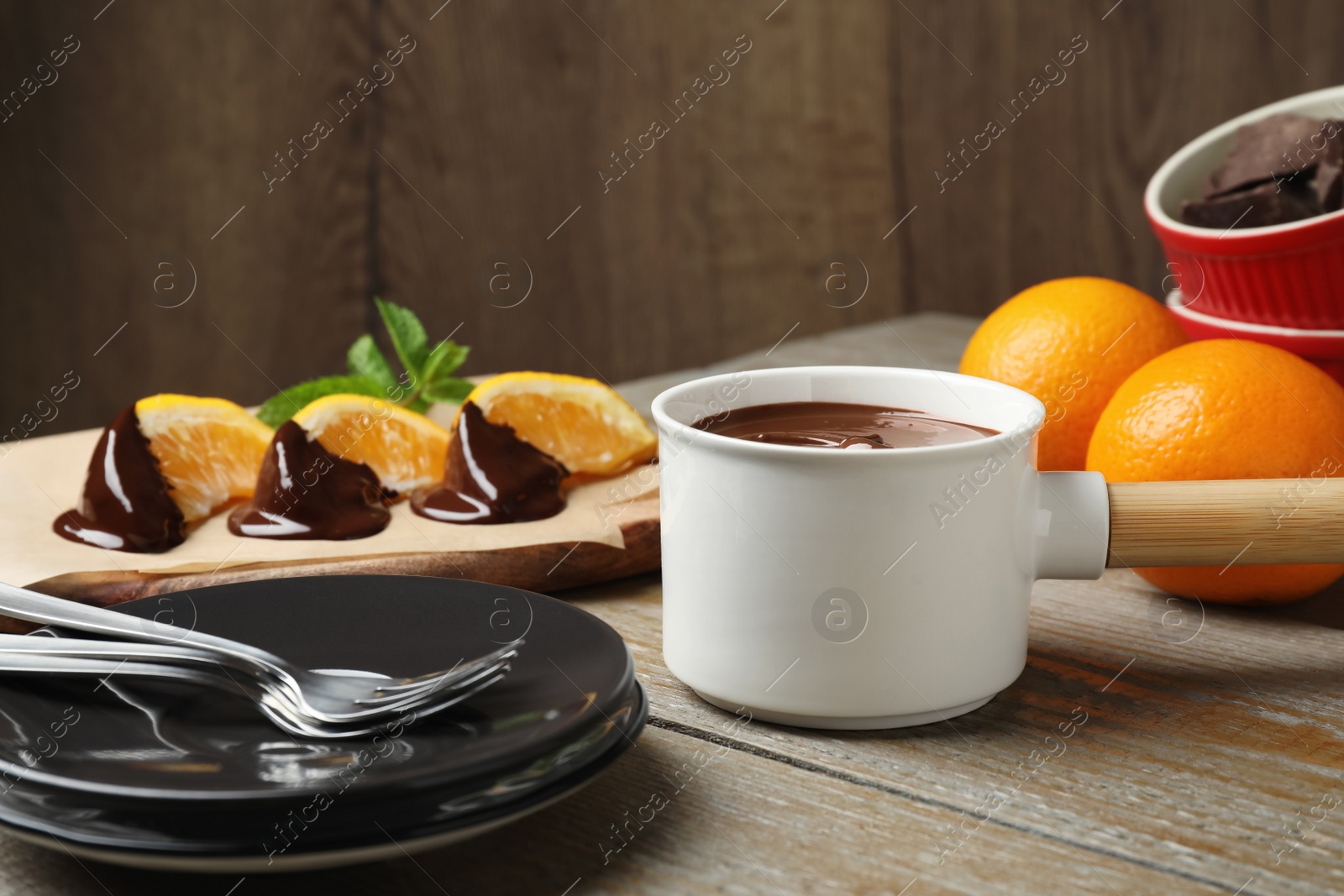 Photo of Fondue pot with milk chocolate and oranges on wooden table