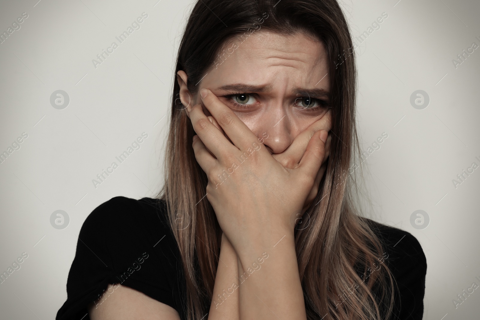Photo of Scared woman covering mouth with her hands on light background. Stop violence
