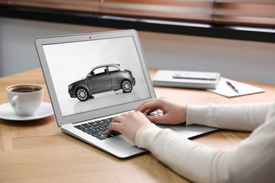 Photo of Woman using laptop to buy car at wooden table indoors, closeup