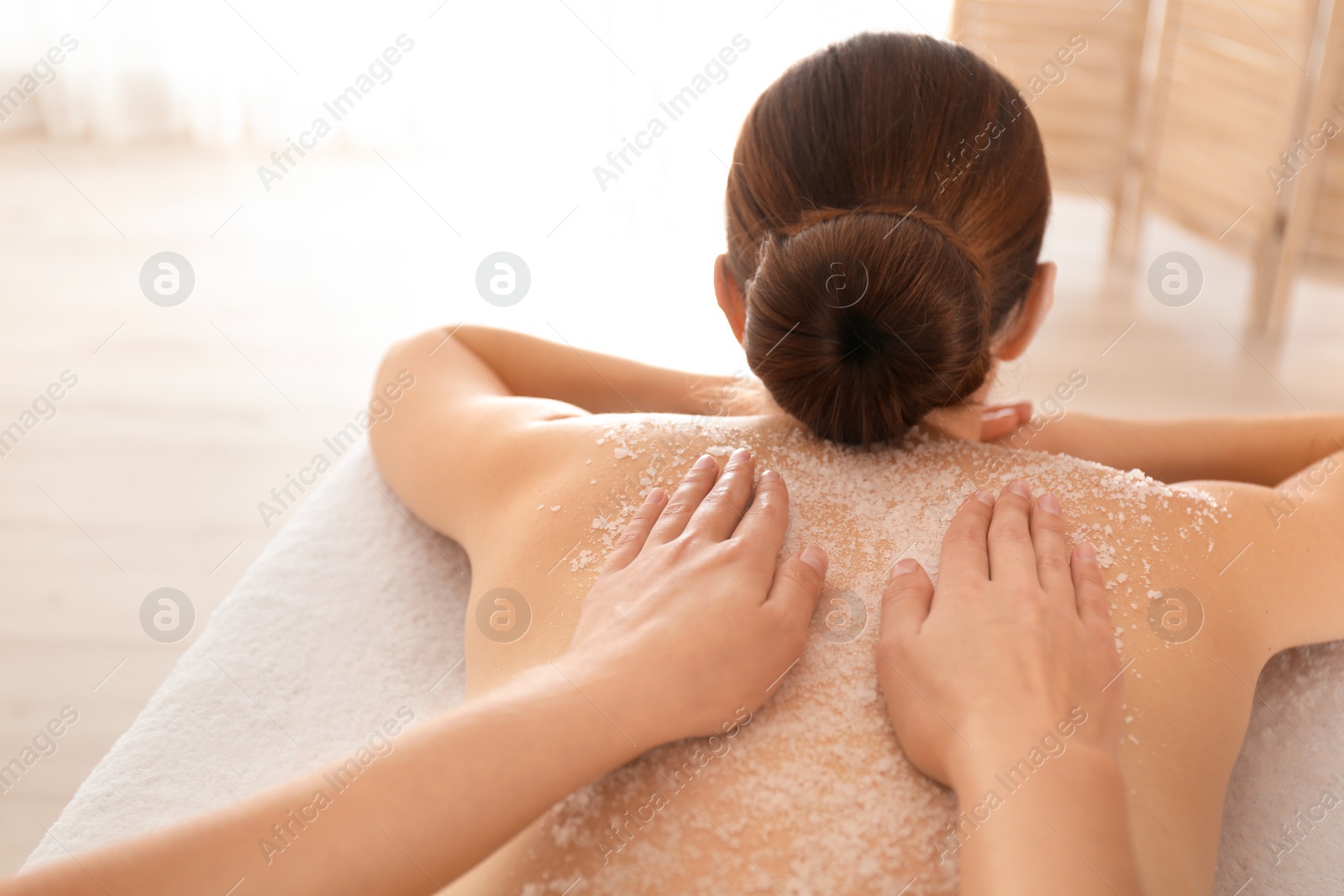 Photo of Young woman having body scrubbing procedure with sea salt in spa salon, closeup