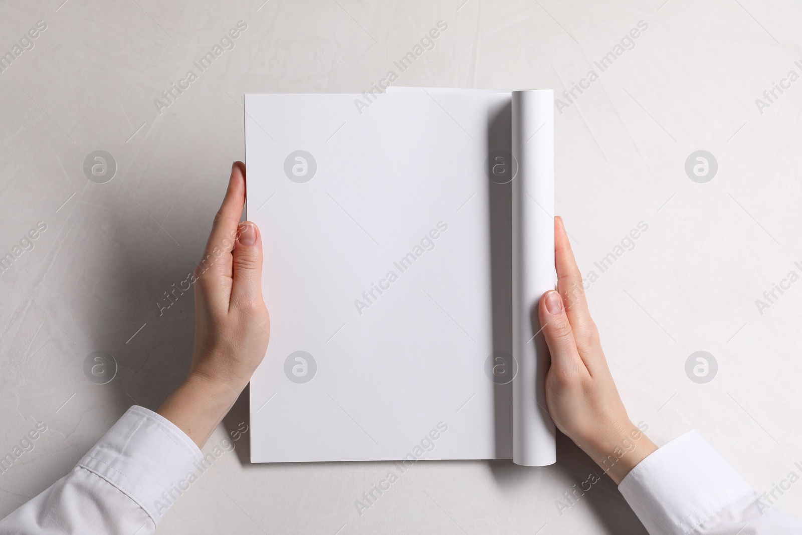 Photo of Woman holding notebook with blank pages at white table, top view. Mockup for design