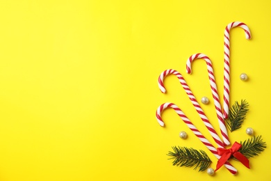 Photo of Flat lay composition with candy canes and fir tree branches on yellow background. Space for text