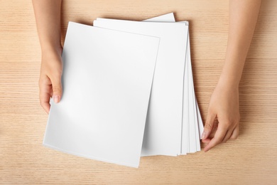 Woman holding blank paper sheets for brochure at wooden table, top view. Mock up