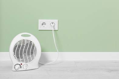 Photo of Electric fan heater near pale green wall indoors. Space for text