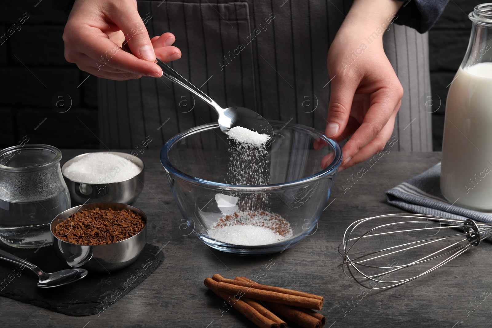 Photo of Making dalgona coffee. Woman pouring sugar into bowl at grey table, closeup