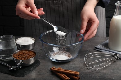 Making dalgona coffee. Woman pouring sugar into bowl at grey table, closeup
