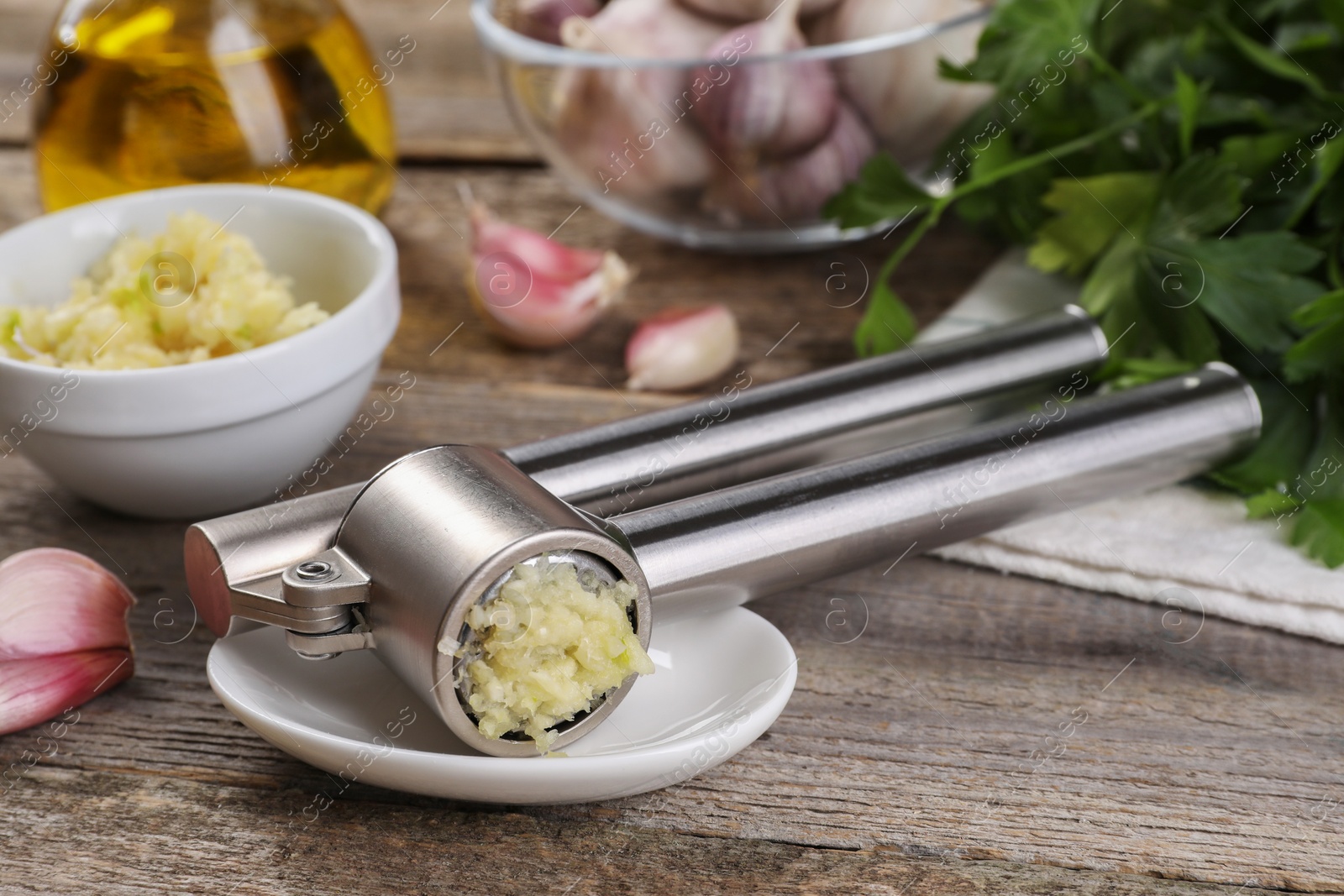 Photo of Garlic press, cloves and mince on wooden table, closeup