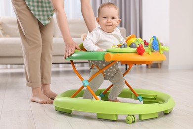 Cute boy making first steps with baby walker. Mother and her little son spending time together at home