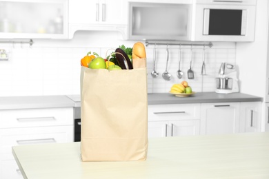 Photo of Paper shopping bag full of vegetables and baguette on table in kitchen. Space for text